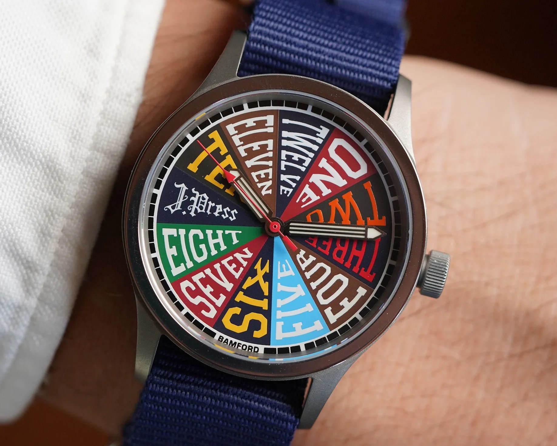 Round wristwatch with a colorful dial displaying numbers as words in various fonts and colors, blue fabric strap.