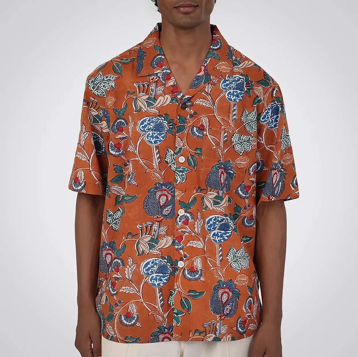 Rust-orange short-sleeve button-up shirt with blue, green, and white floral print worn by a person.