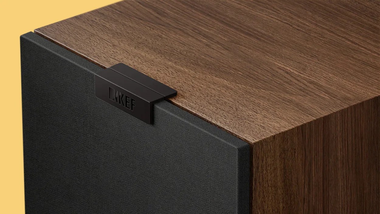 Wood-finished KEF speaker with black fabric grille and KEF logo on a yellow background.