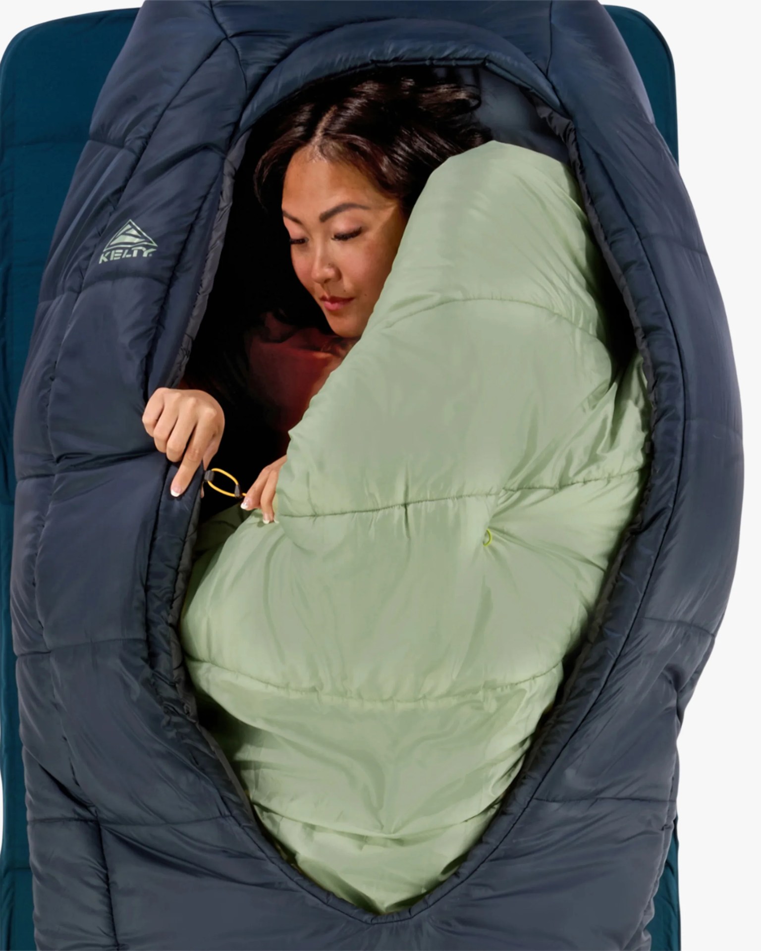 Person inside a navy blue Kelty sleeping bag with a light green inner lining, lying on a blue sleeping pad.