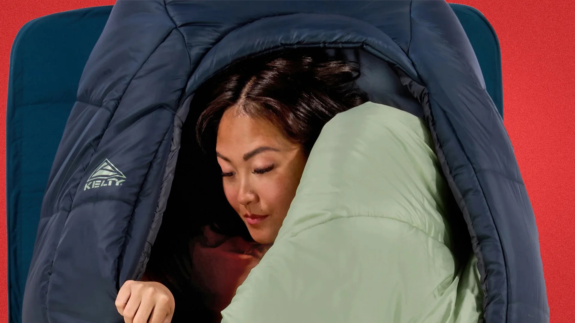 Person inside a navy blue Kelty sleeping bag with a light green inner lining on a blue sleeping pad.