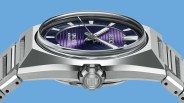 Close-up of a stainless steel Seiko wristwatch with a purple dial and silver hands against a blue background.