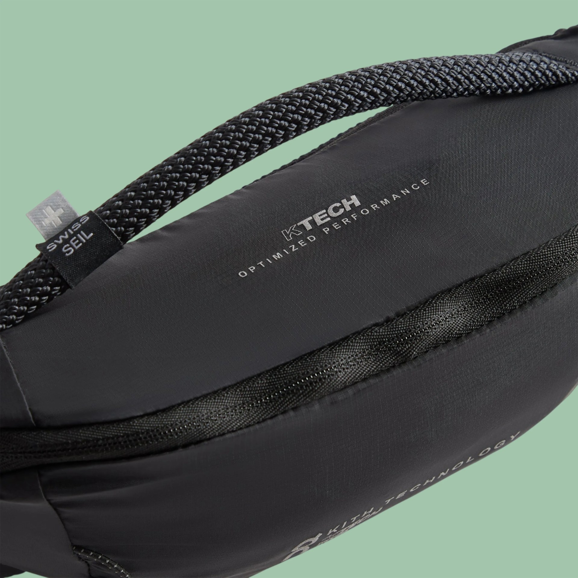 Close-up of a black bag with a braided handle, "KTECH Optimized Performance" text, and a "Swiss Seil" tag on a green background.