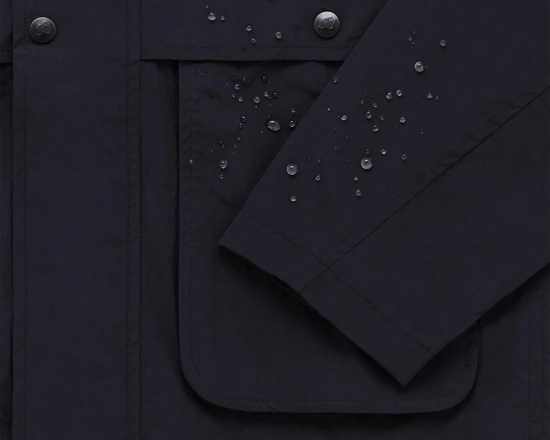 Close-up of navy blue water-resistant jacket sleeve and pocket with water droplets on the fabric.