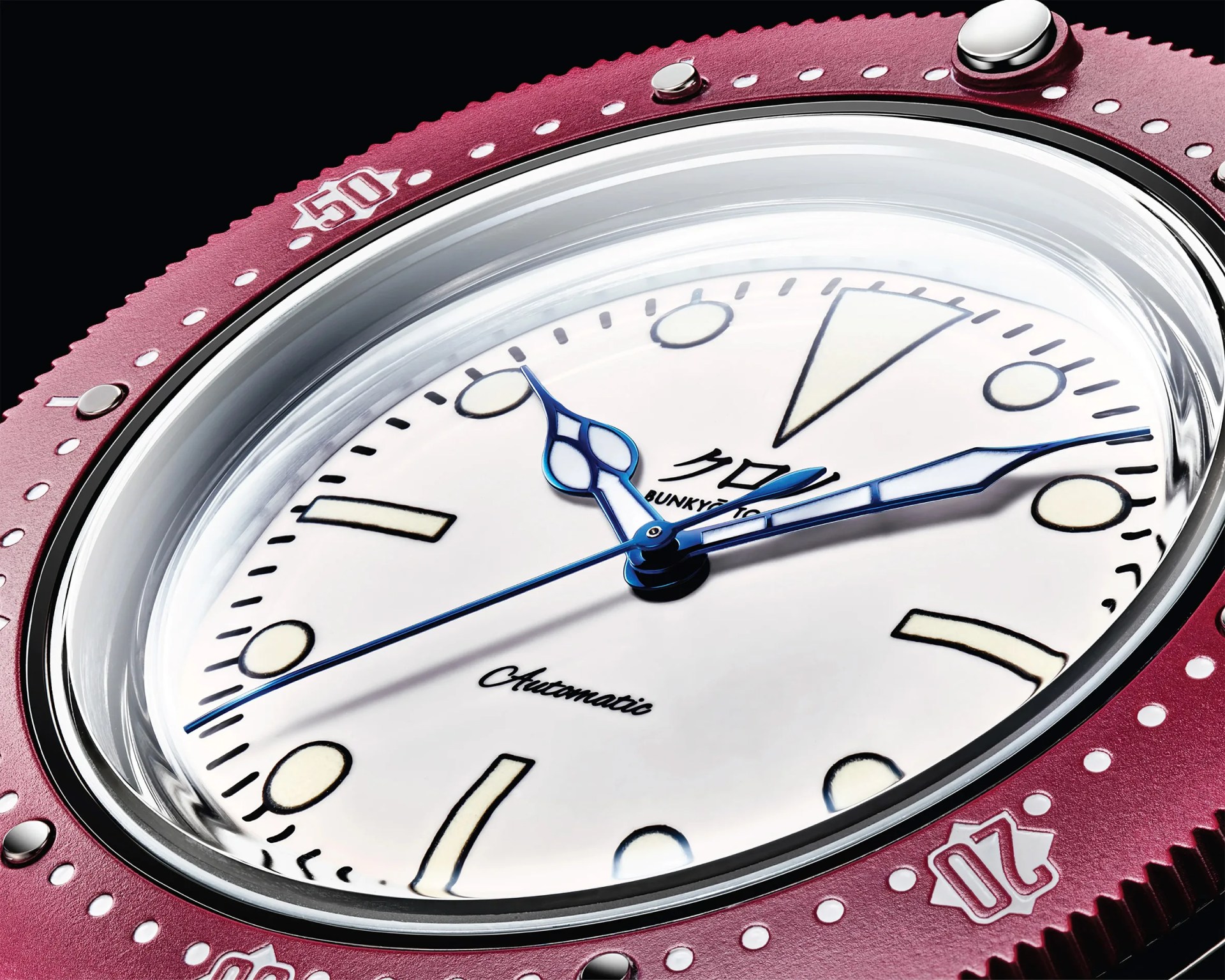 Close-up of a watch face with a white dial, blue ornate hands, and a red bezel marked with minute indicators.