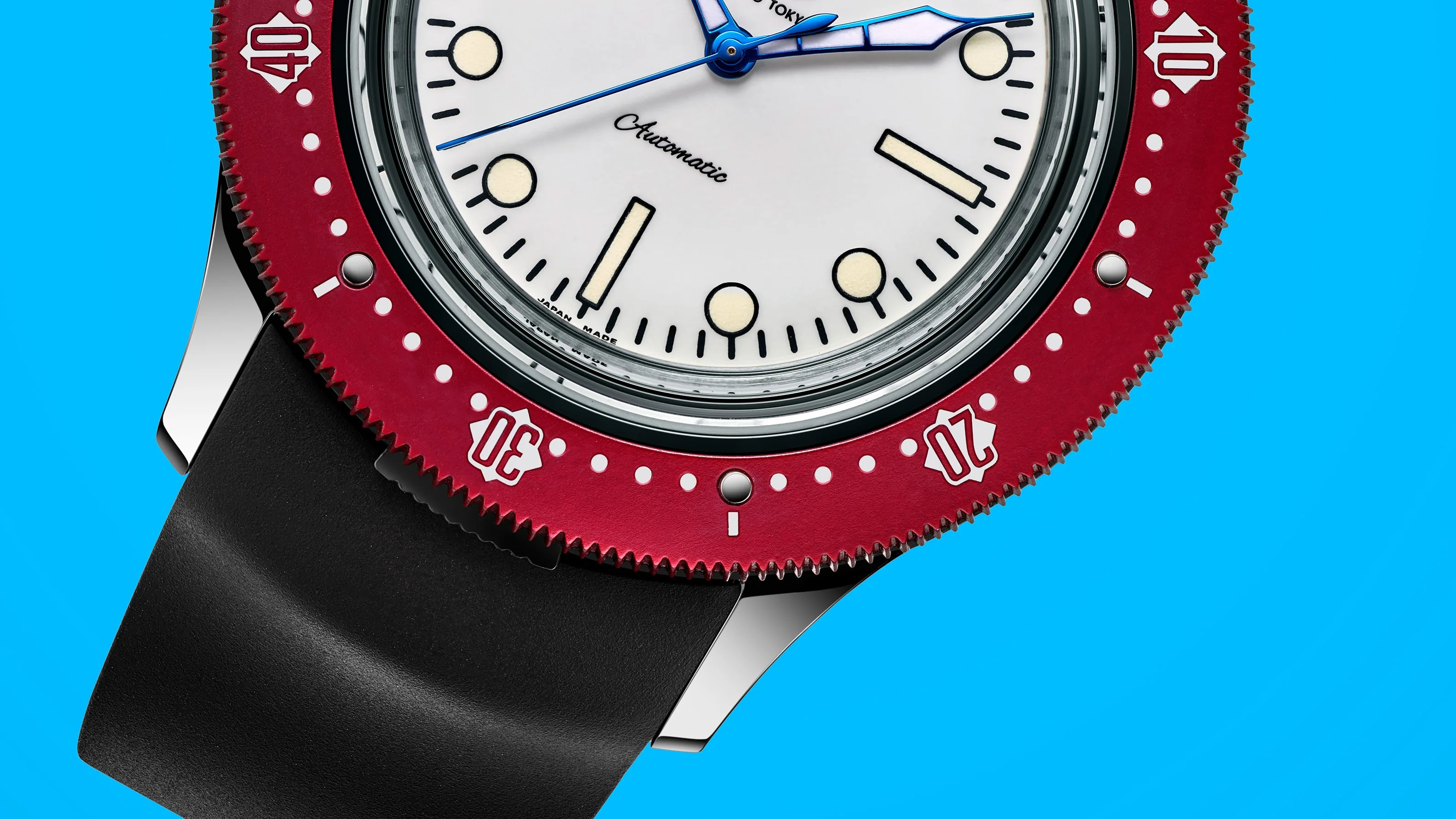 Close-up of a wristwatch with a white dial, blue hands, red bezel with white markings, and black strap on a blue background.