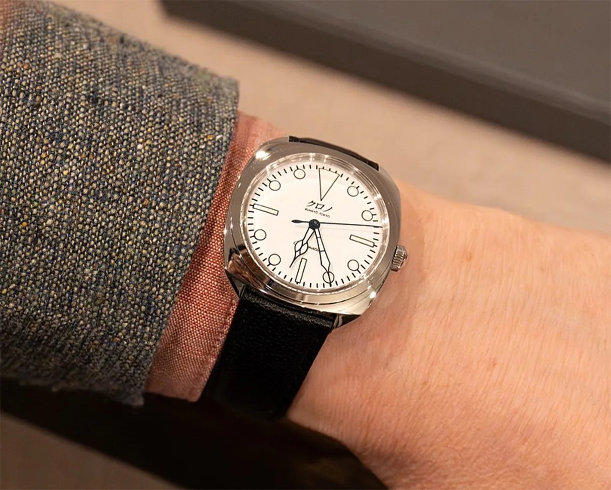 Silver wristwatch with a white dial, black leather strap, and Japanese characters on the face worn on a wrist.