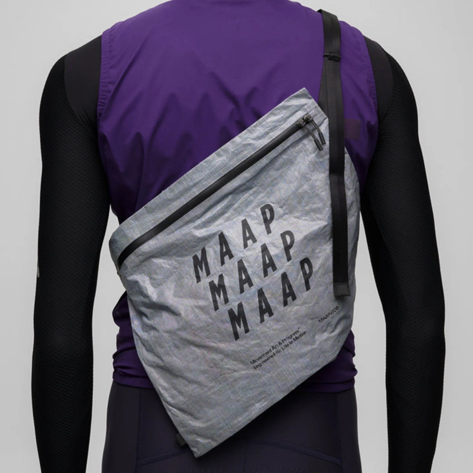 Gray crossbody bag with black zipper and "MAAP" text worn over a purple and black long-sleeve outfit.