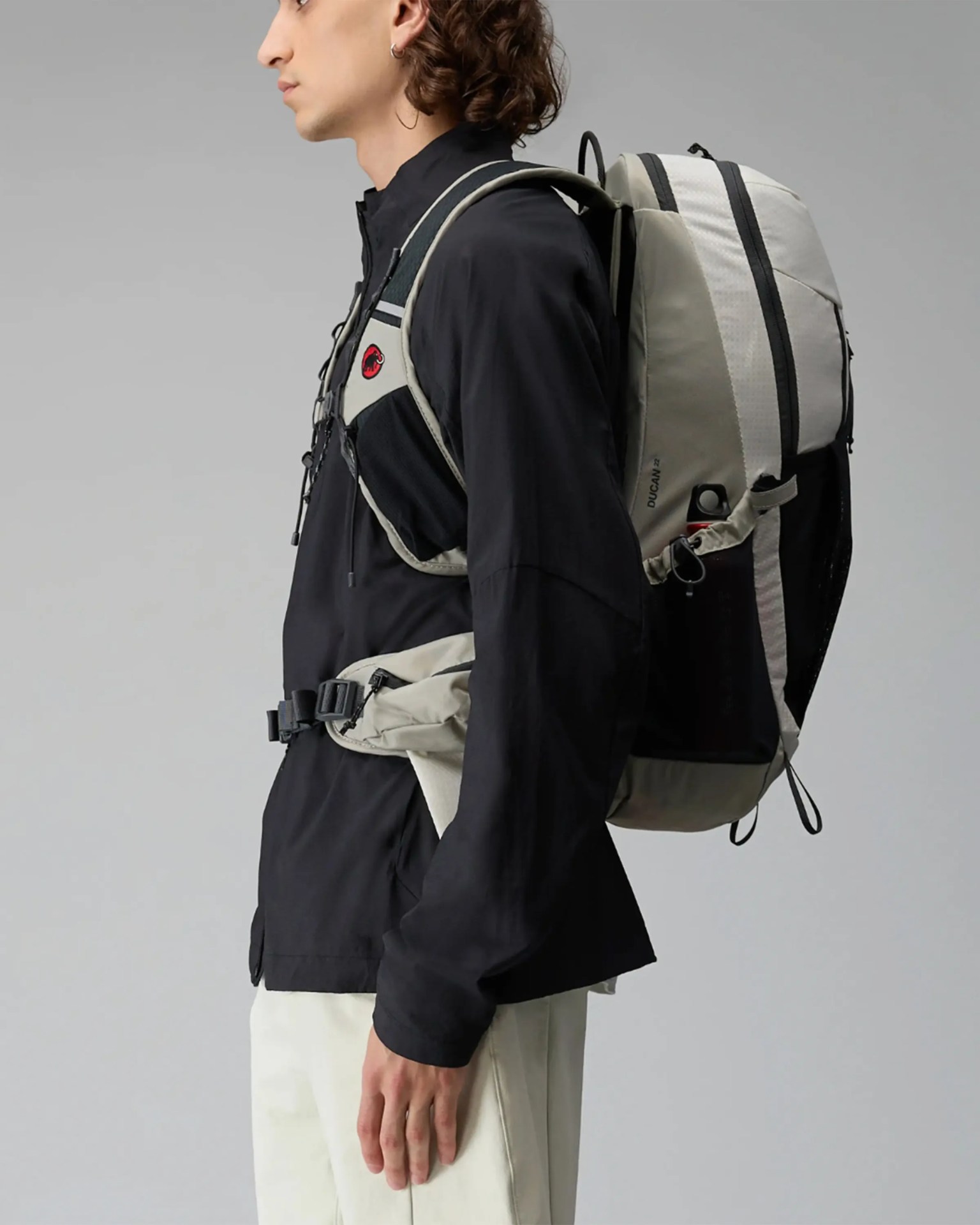 Light gray and black hiking backpack with multiple straps worn by a person in a black jacket and white pants.