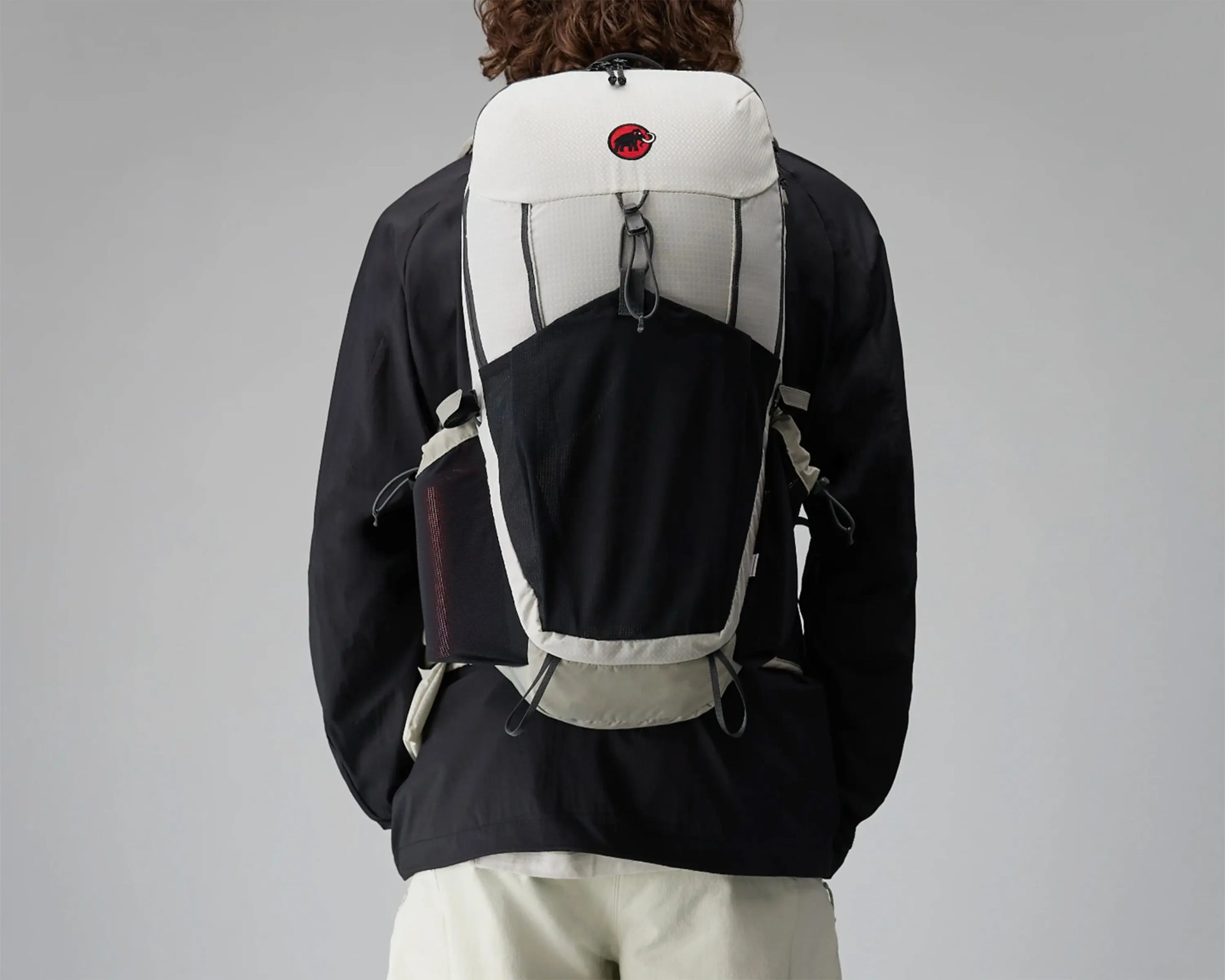 Light gray and black hiking backpack with red logo worn by a person in a black jacket and light pants.