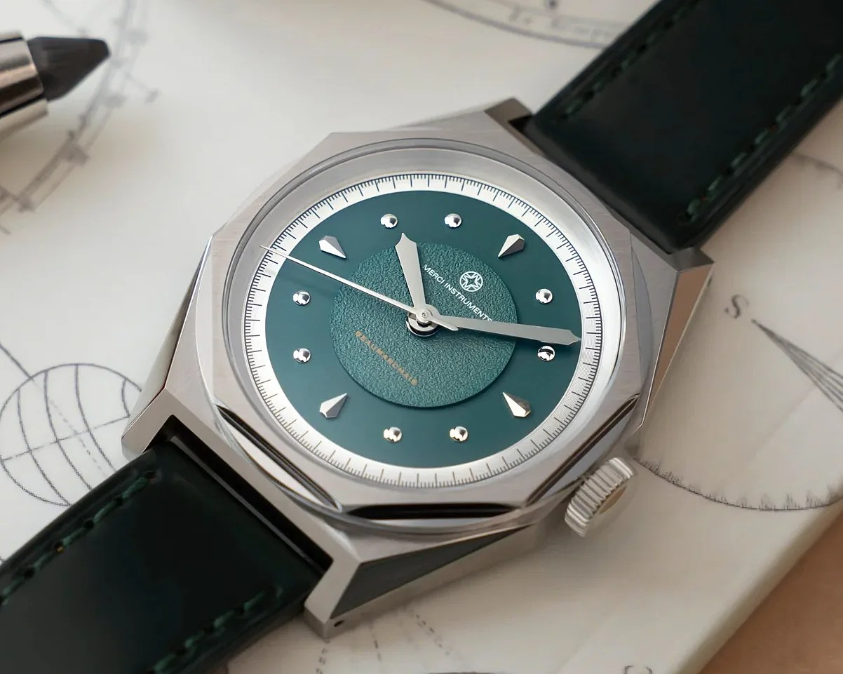 Close-up of a silver octagonal wristwatch with a textured green dial and dark green leather strap on a paper with sketches.