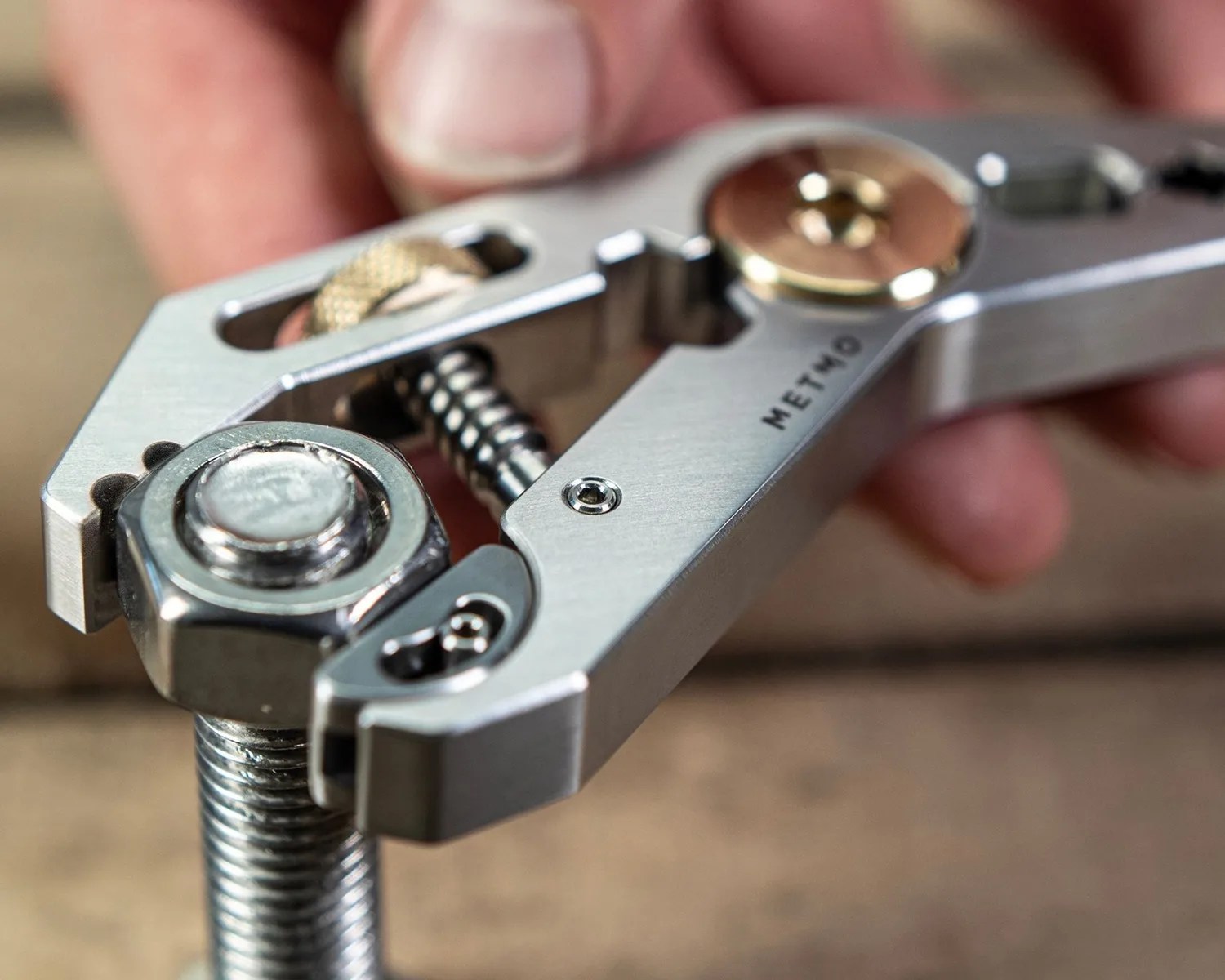 Close-up of a silver adjustable wrench gripping a large bolt with a nut, held by a hand.