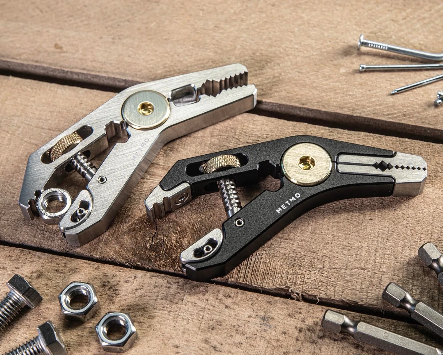 Two compact multi-tool pliers, one silver and one black with gold accents, on a wooden surface with screws and nuts nearby.