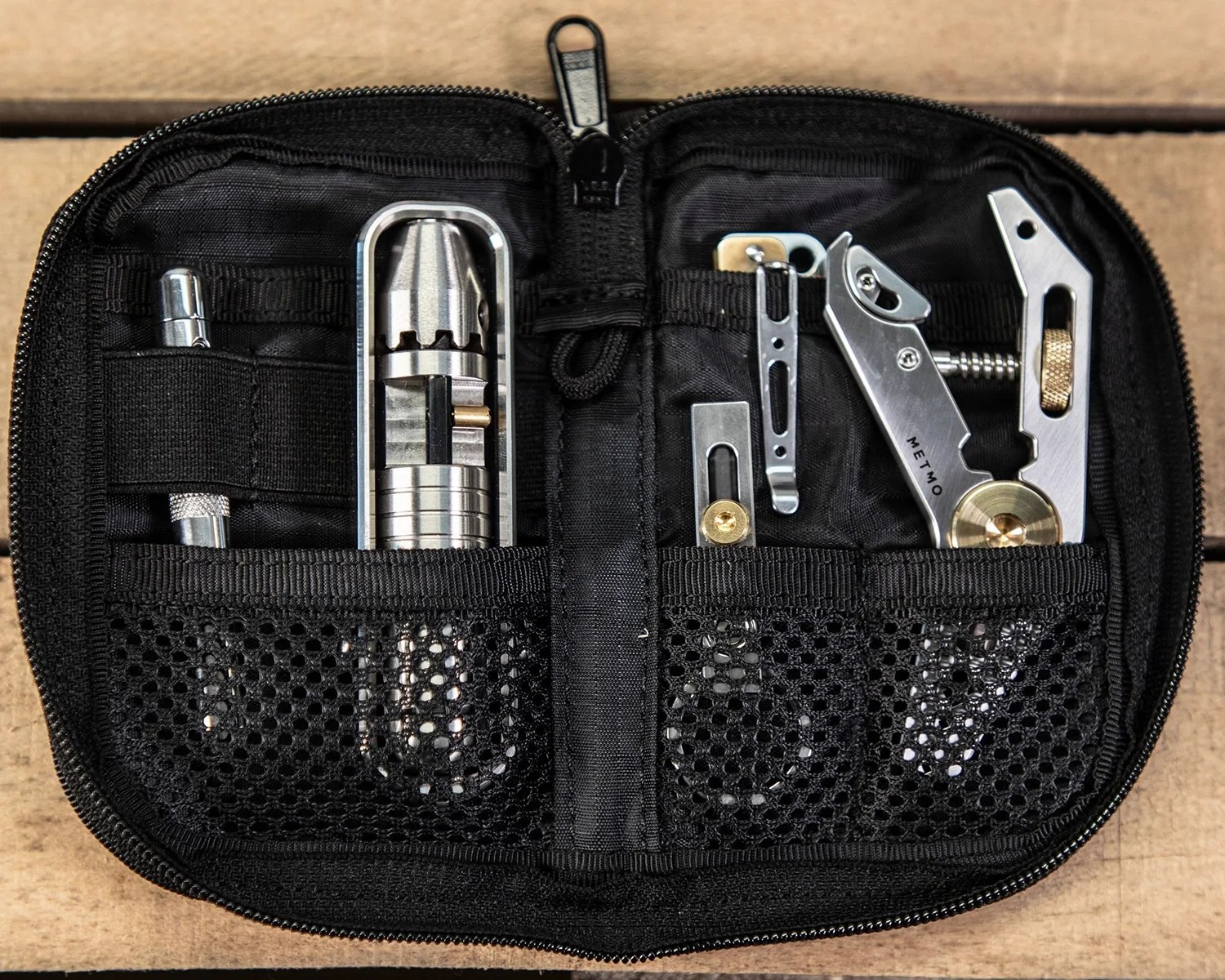 Black zippered pouch with organized silver metal multitools and accessories inside.