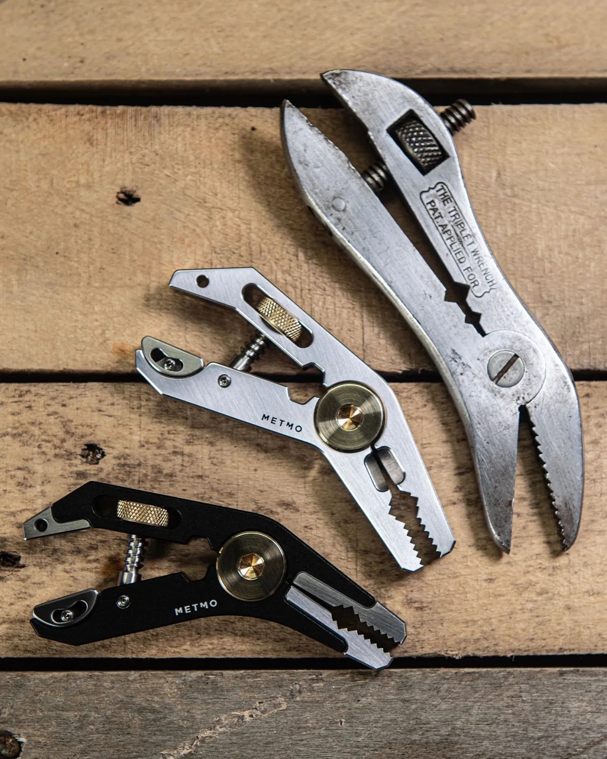 Three adjustable metal wrenches, two labeled METMO in black and silver finishes, on a wooden surface.