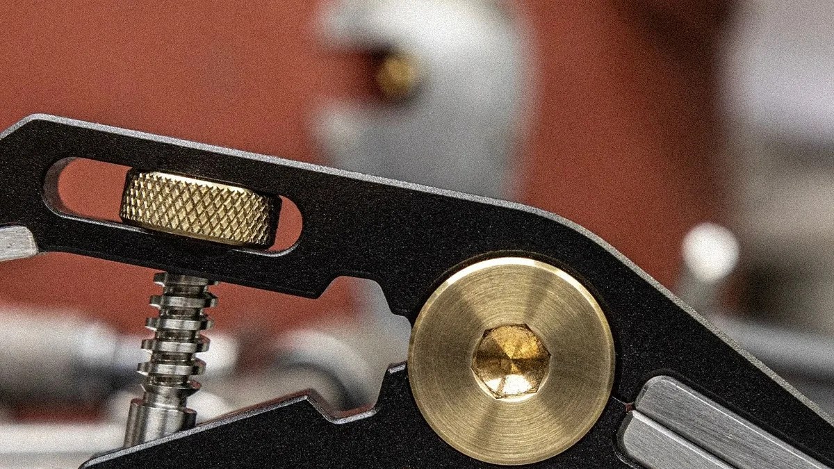 Close-up of a black metal tool with a knurled brass adjustment knob and a brass hex screw.