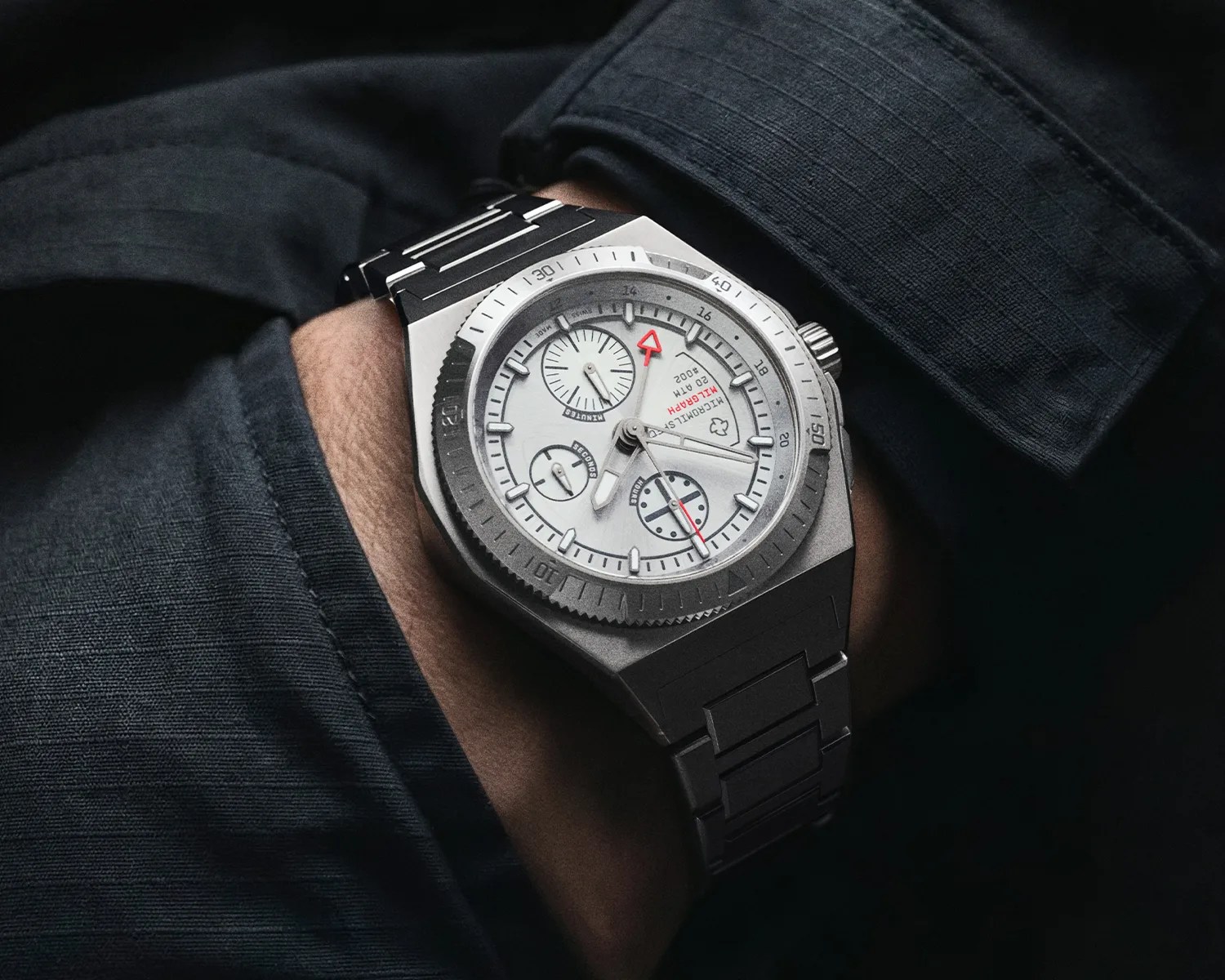 Silver metal wristwatch with white dial, red accents, and multiple subdials worn on a wrist with dark clothing.
