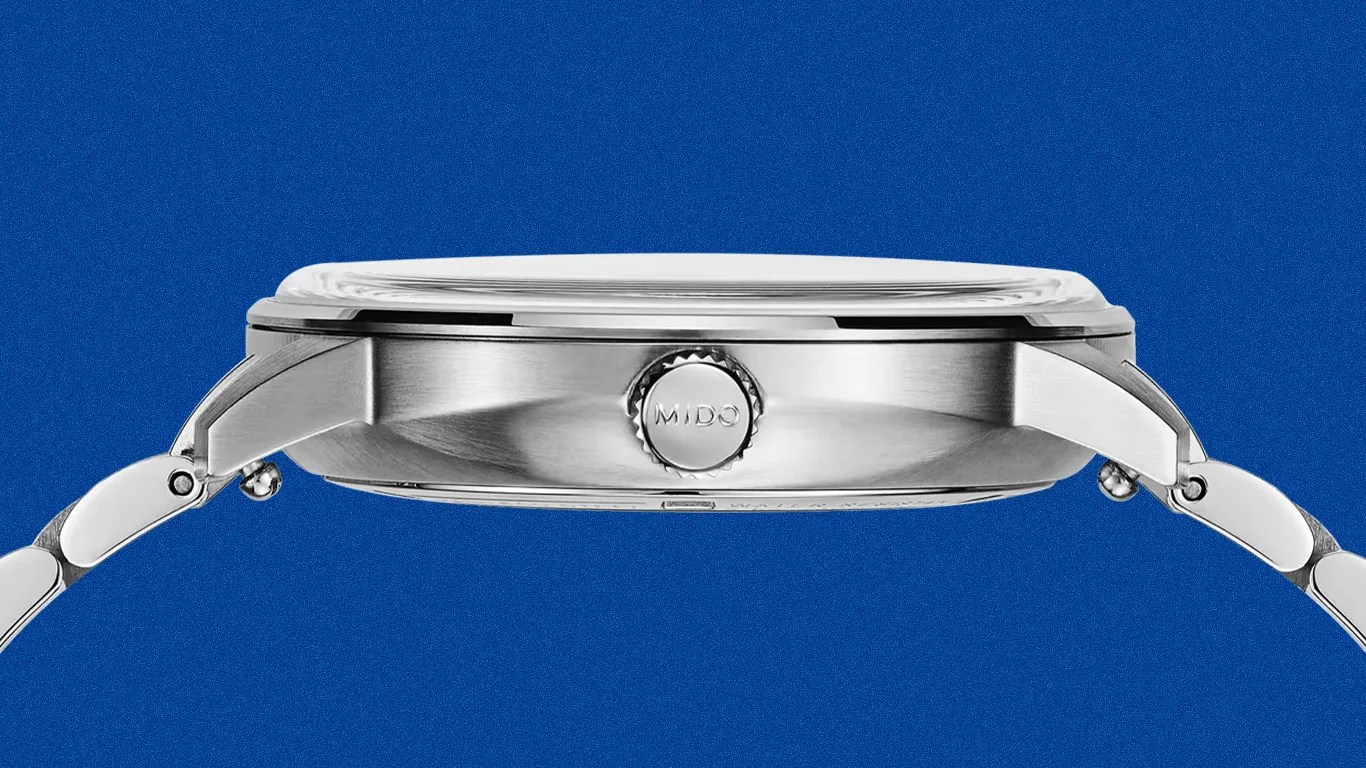 Side view of a silver Mido wristwatch with a metal bracelet against a blue background.