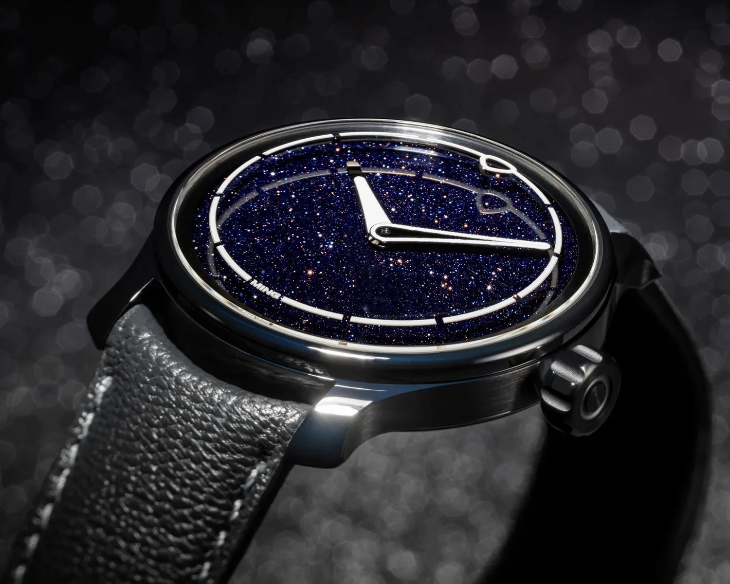Close-up of a wristwatch with a sparkling deep blue starry dial, black case, and black leather strap.