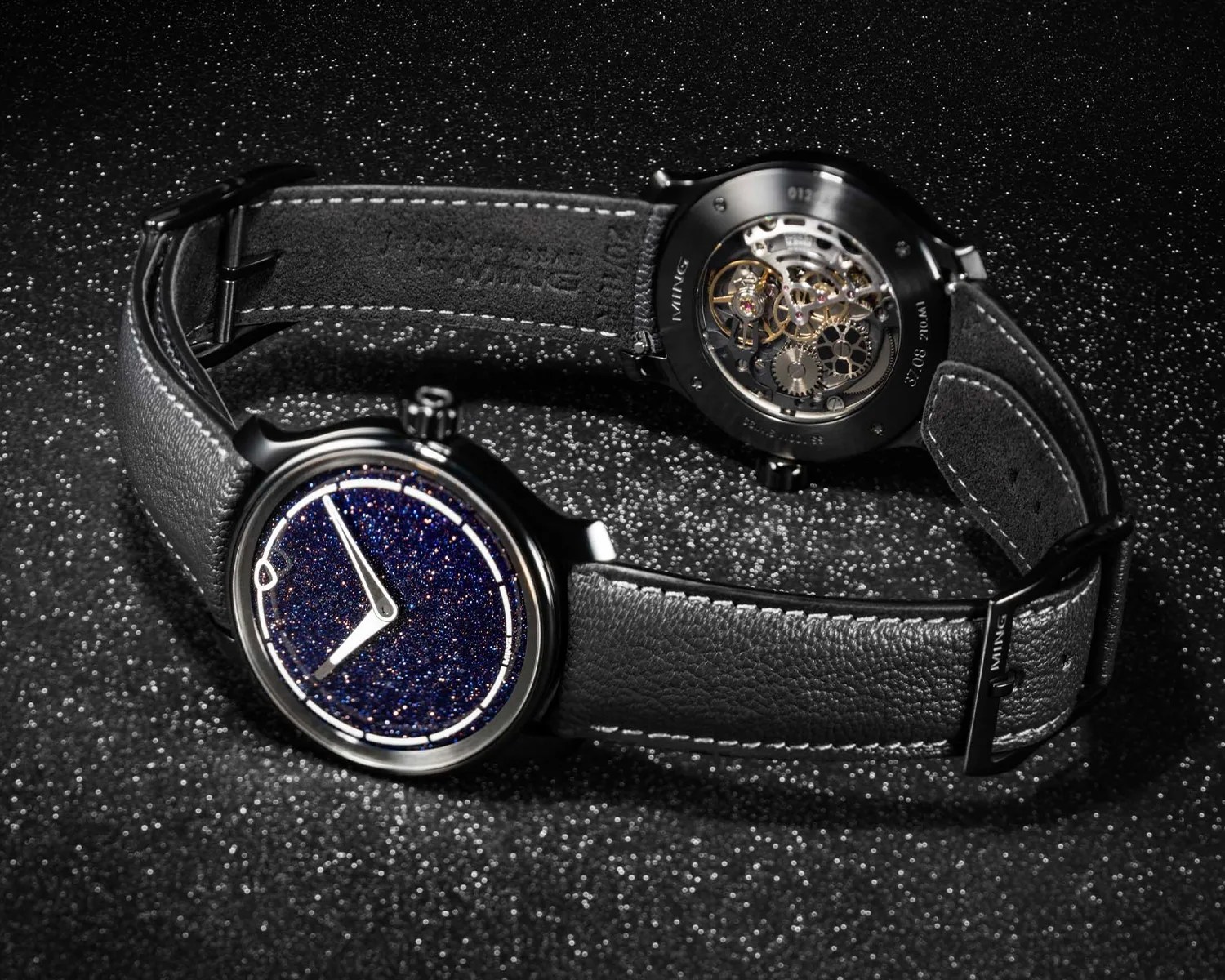 Black leather wristwatch with a sparkling dark blue dial and visible mechanical movement on the back.