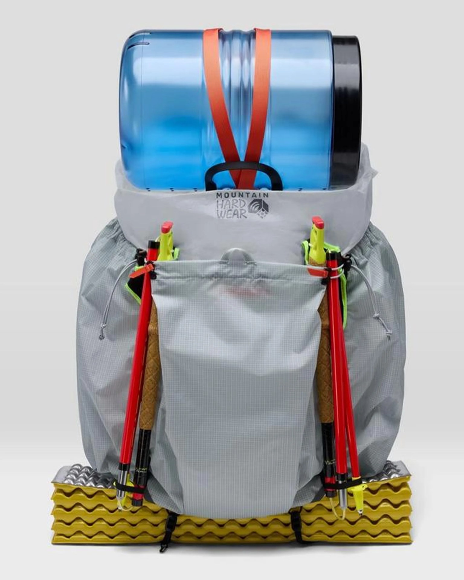 Gray Mountain Hardwear backpack with blue water container strapped on top, red trekking poles on sides, and yellow foam sleeping pad attached at the bottom.