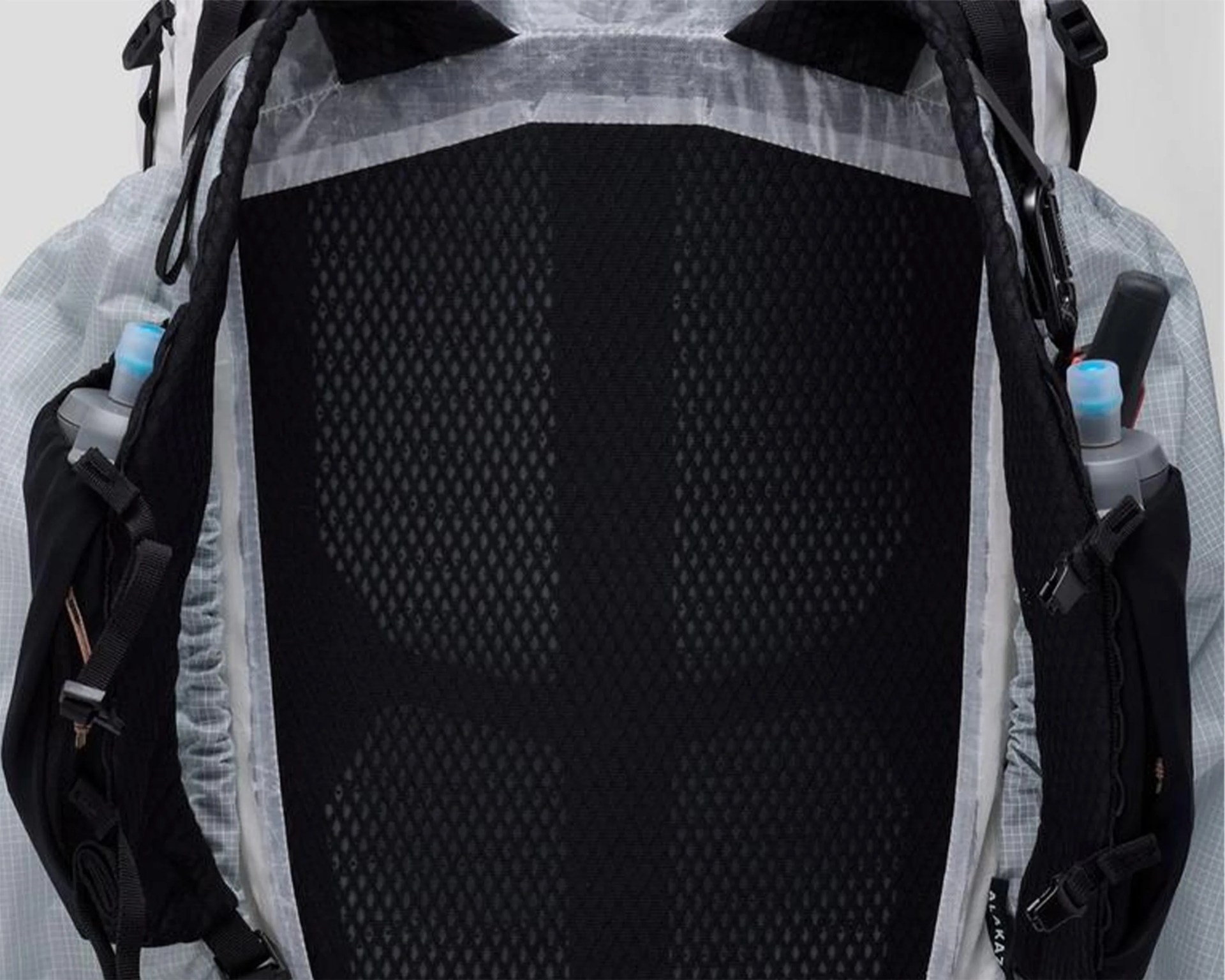 Close-up of a black mesh back panel on a light gray backpack with side pockets holding water bottles.