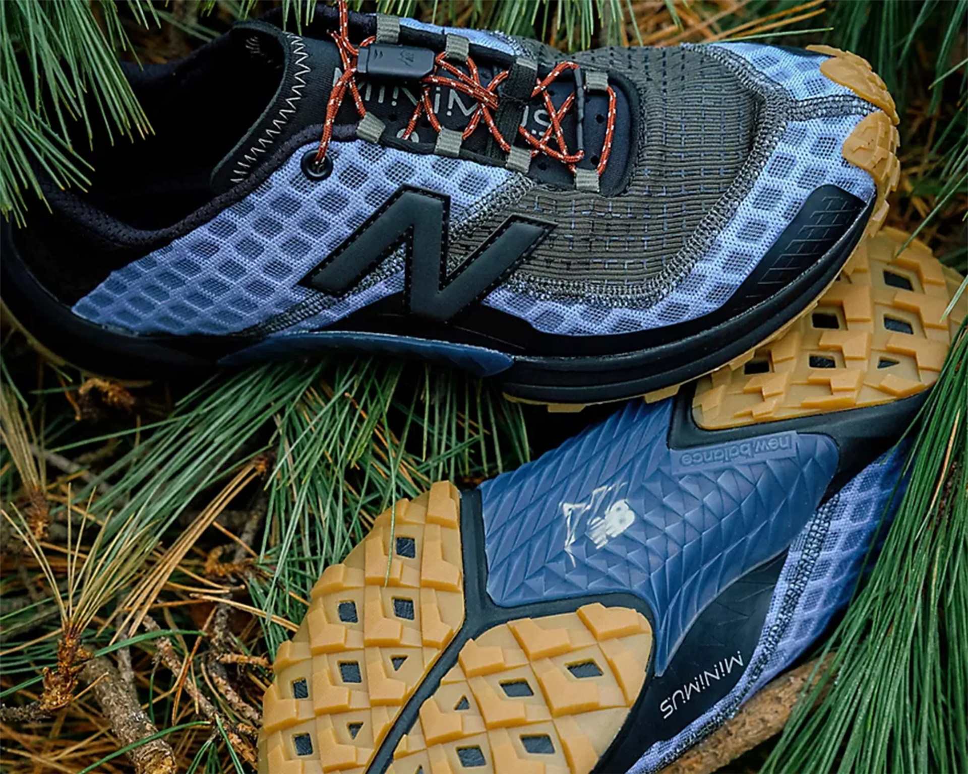 Pair of blue and black New Balance Minimus trail running shoes with tan rubber soles on pine needles.