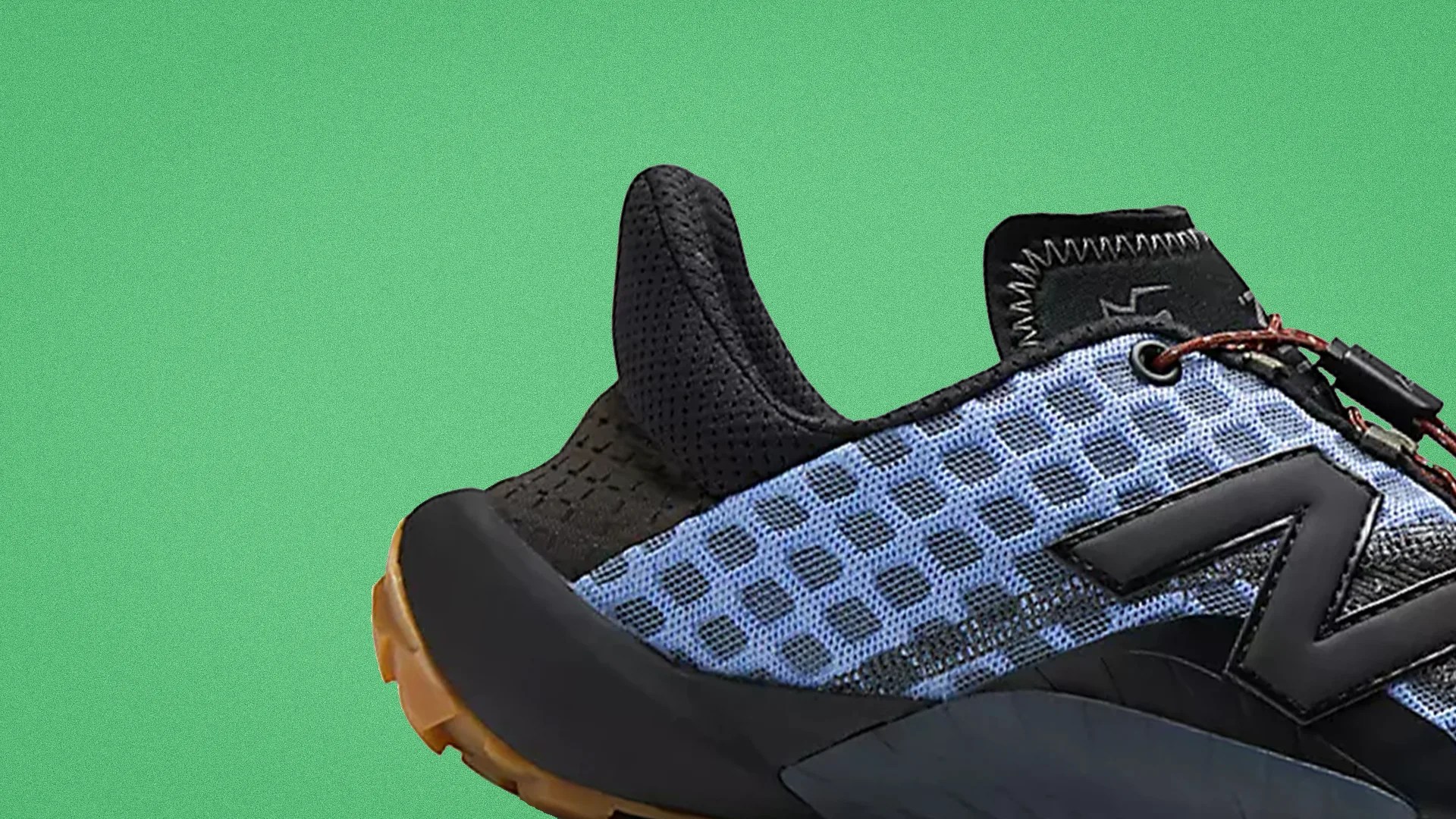 Close-up of a blue and black athletic shoe with a textured mesh upper and a gum sole against a green background.