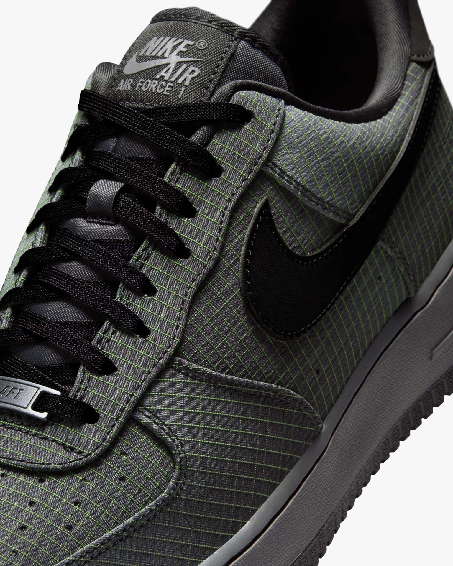 Close-up of a gray Nike Air Force 1 sneaker with black laces, black swoosh, and a grid pattern on the upper.