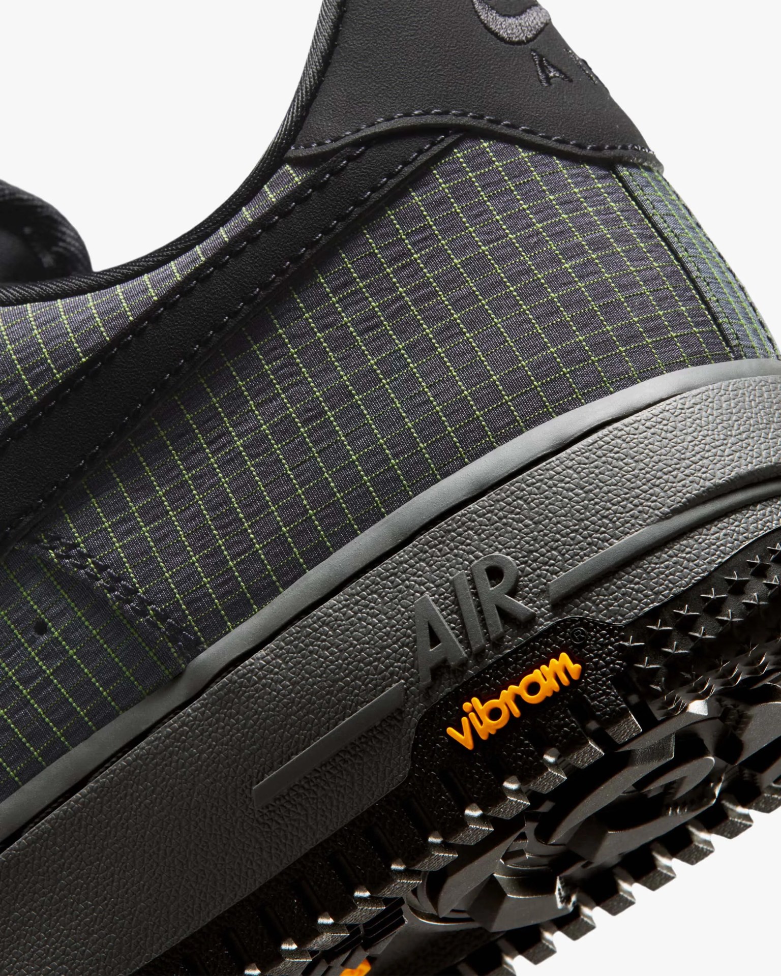 Close-up of a black sneaker heel with green grid pattern, "AIR" embossed on midsole, and orange "vibram" logo on the outsole.