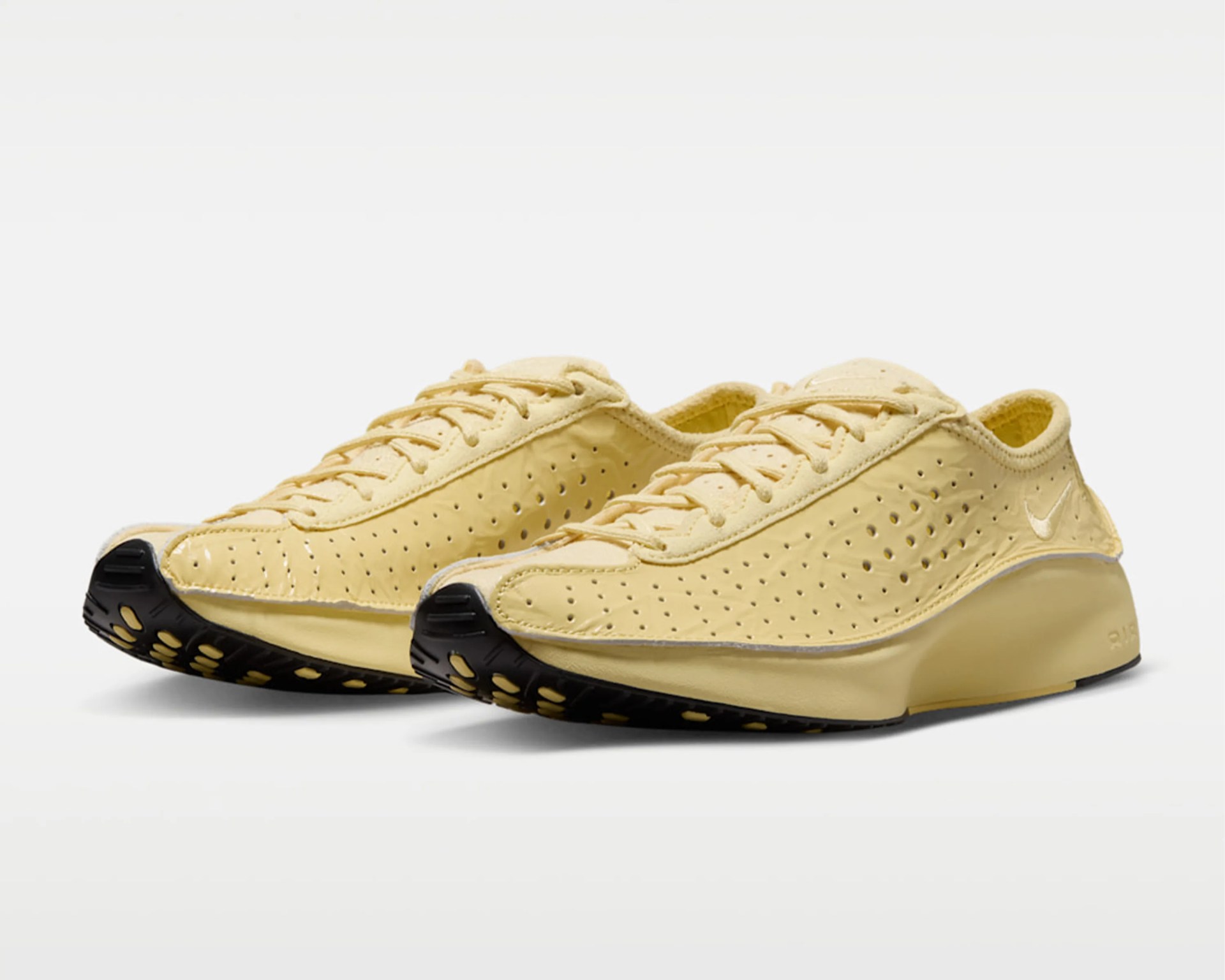Pair of pale yellow perforated Nike sneakers with black soles on a white background.