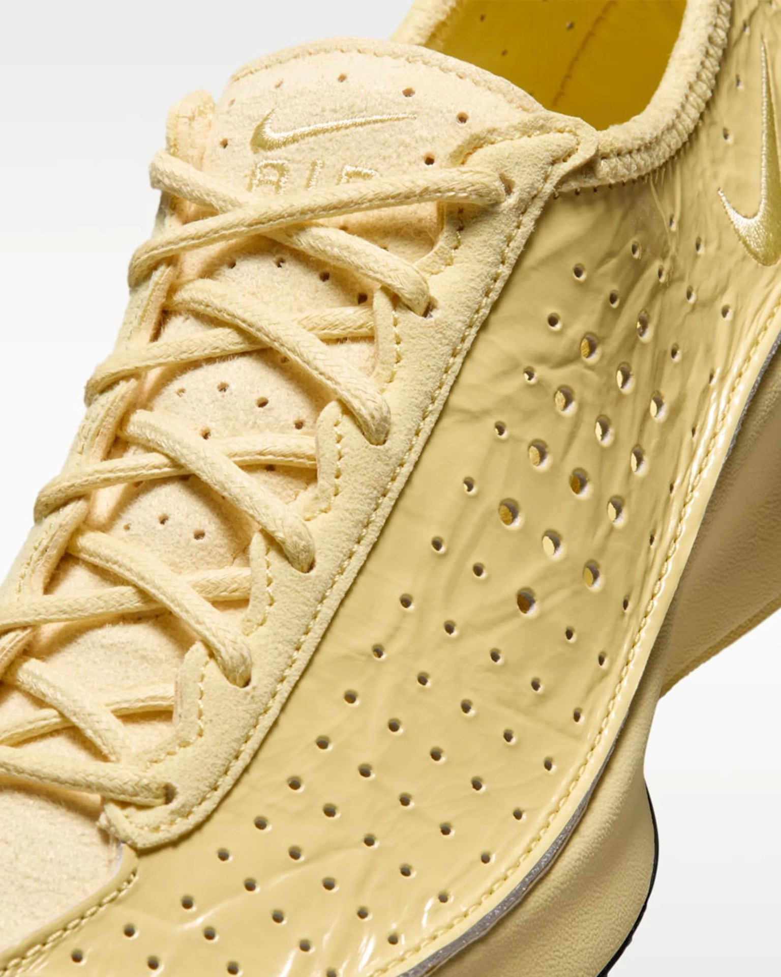 Close-up of a yellow Nike Air sneaker with suede tongue and perforated synthetic side panel.