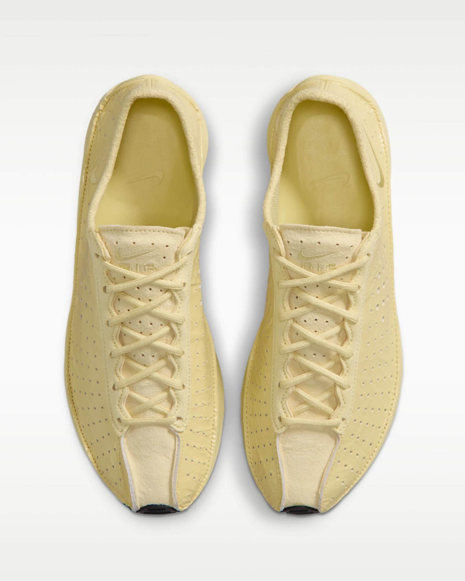 Pair of pale yellow Nike Air sneakers with perforated sides and laces, viewed from above.