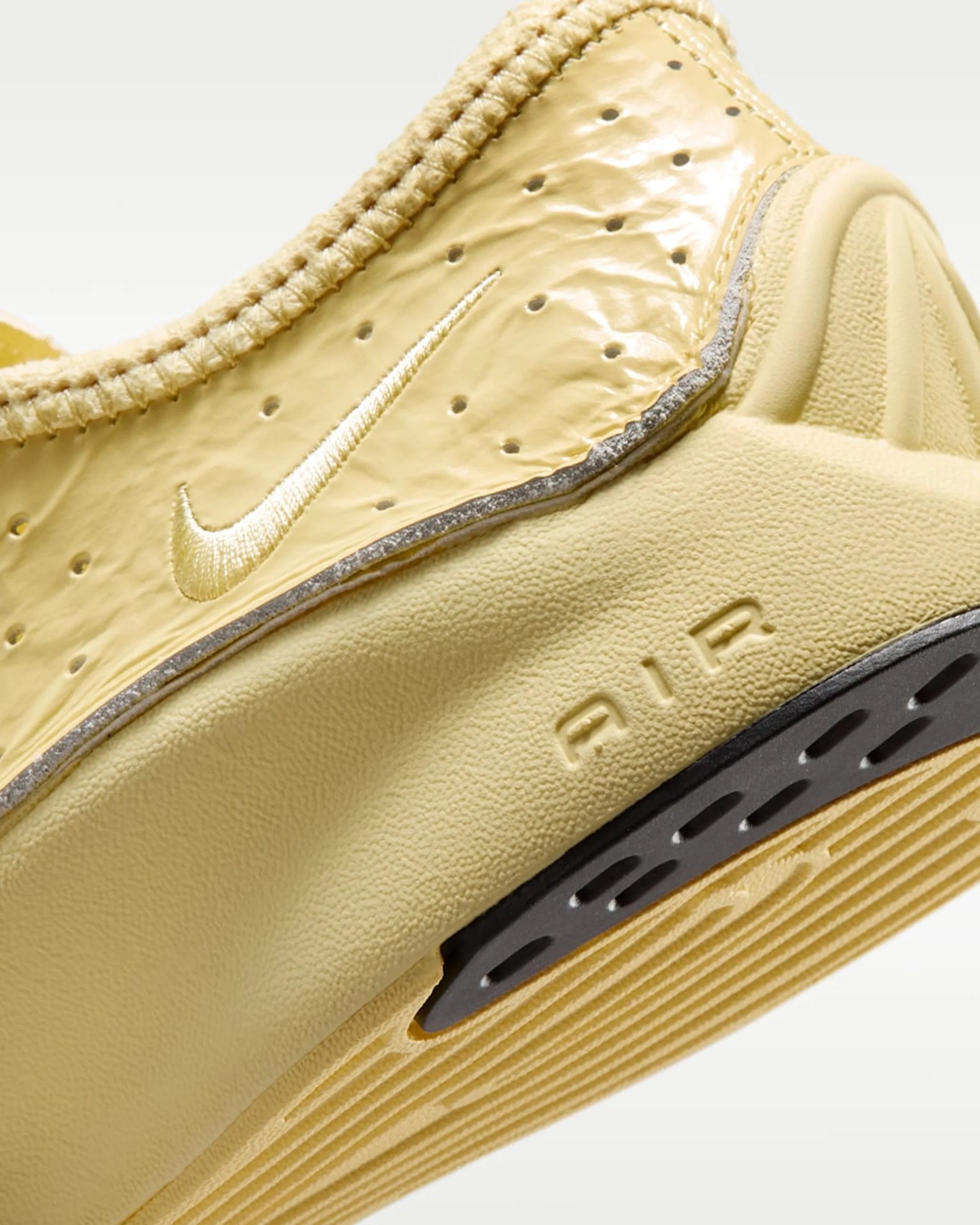 Close-up of the heel area of a yellow Nike Air sneaker with a textured sole and embroidered swoosh logo.