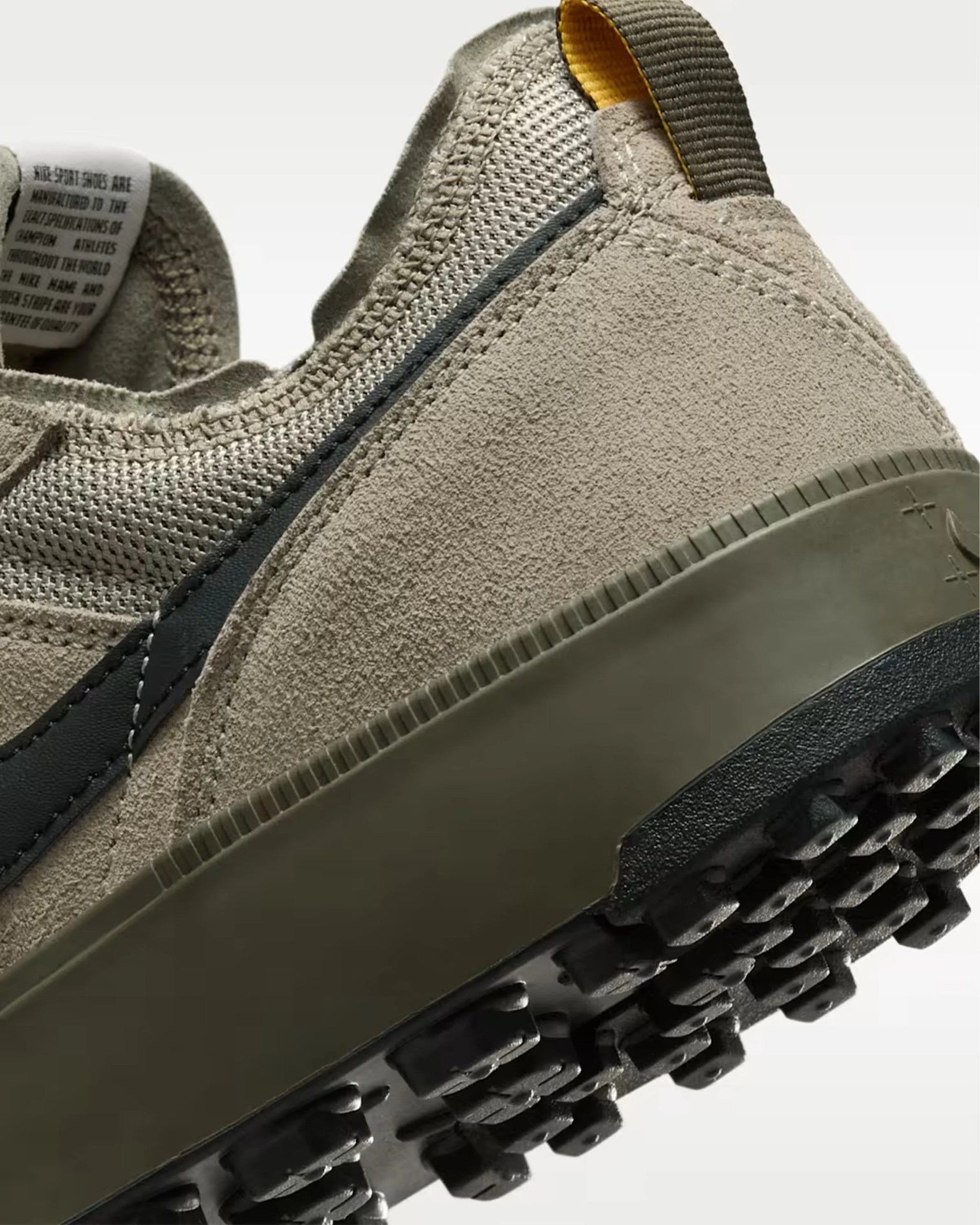 Close-up of the back and sole of a beige suede and mesh sneaker with a black rubber tread and olive midsole.