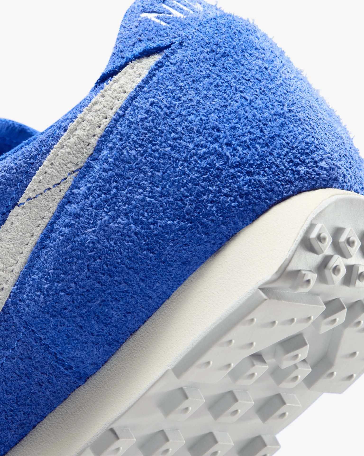 Close-up of a blue suede sneaker heel with a white rubber sole featuring square studs.