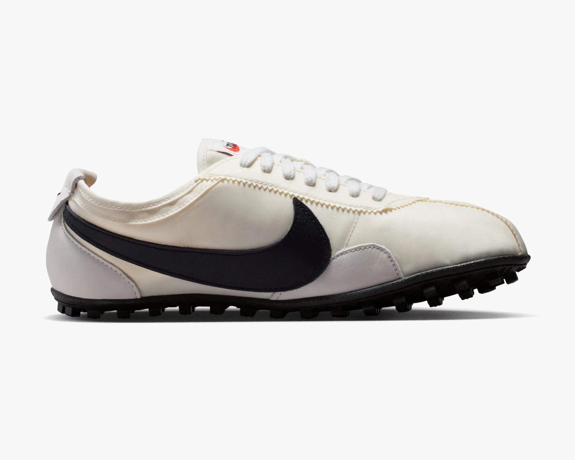 Off-white low-top Nike sneaker with black swoosh logo and black studded sole.