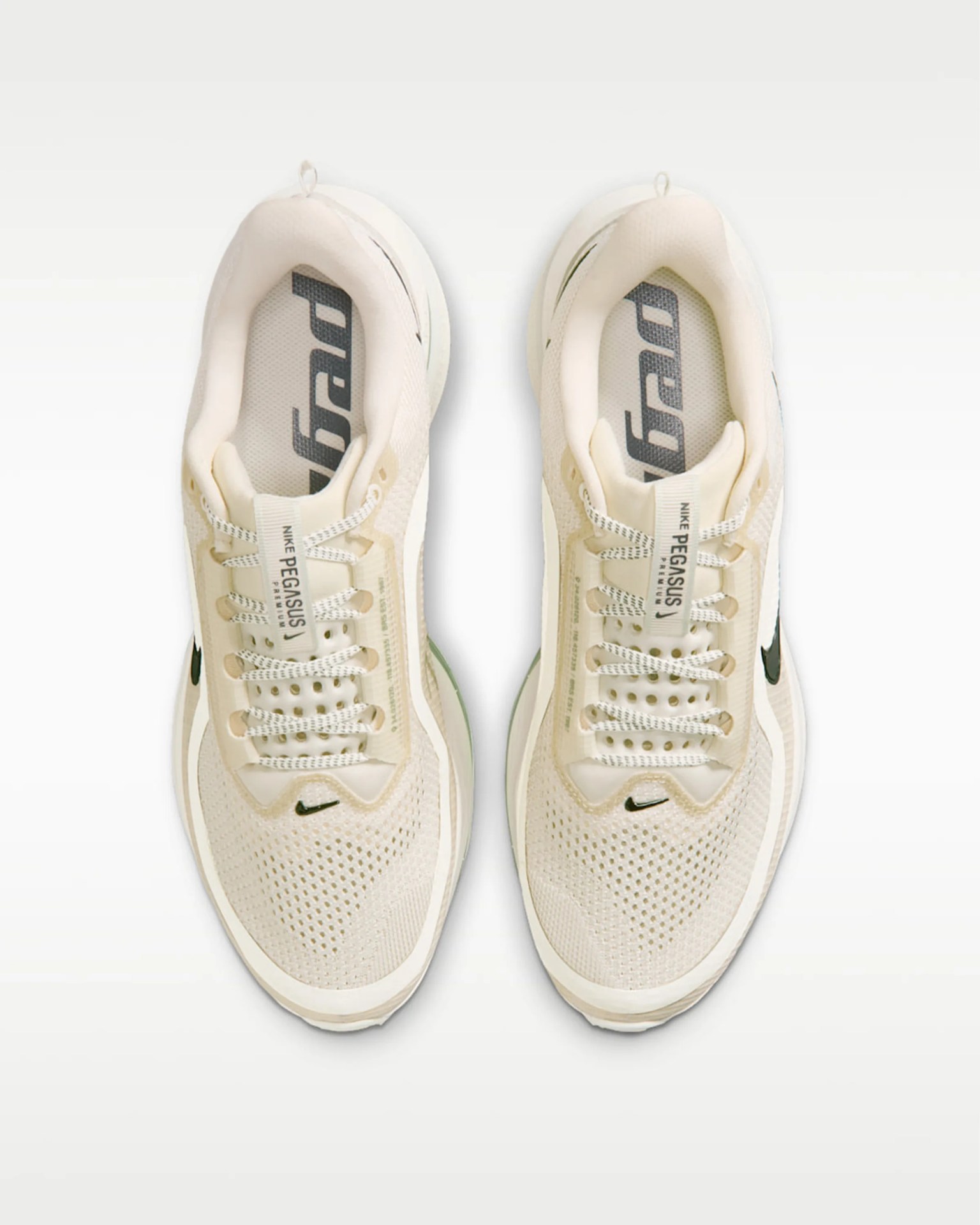 Pair of beige Nike Pegasus running shoes with black swoosh logos and white patterned laces, viewed from above.