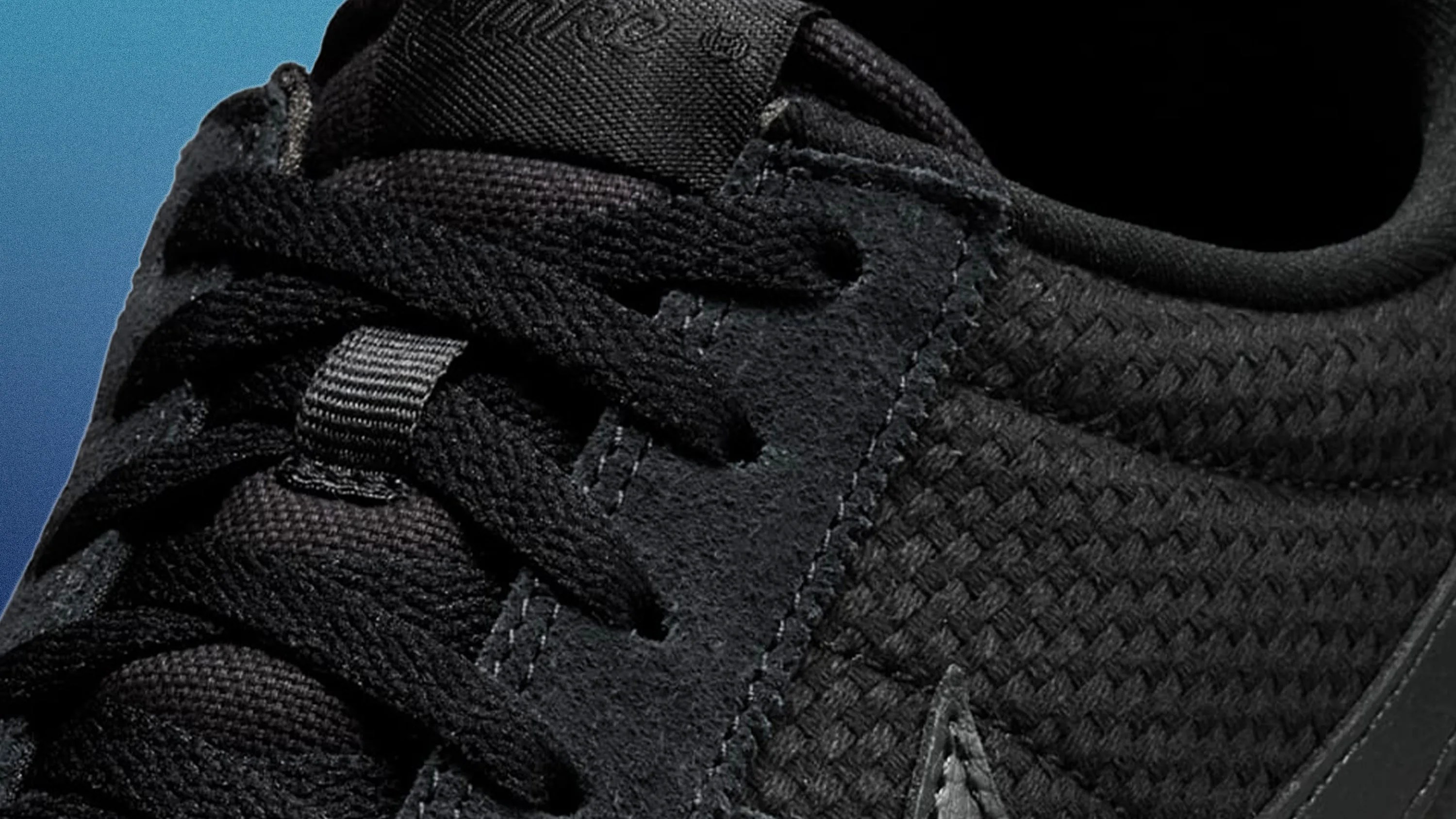 Close-up of black sneaker with woven fabric and suede details, showing laces and stitching.