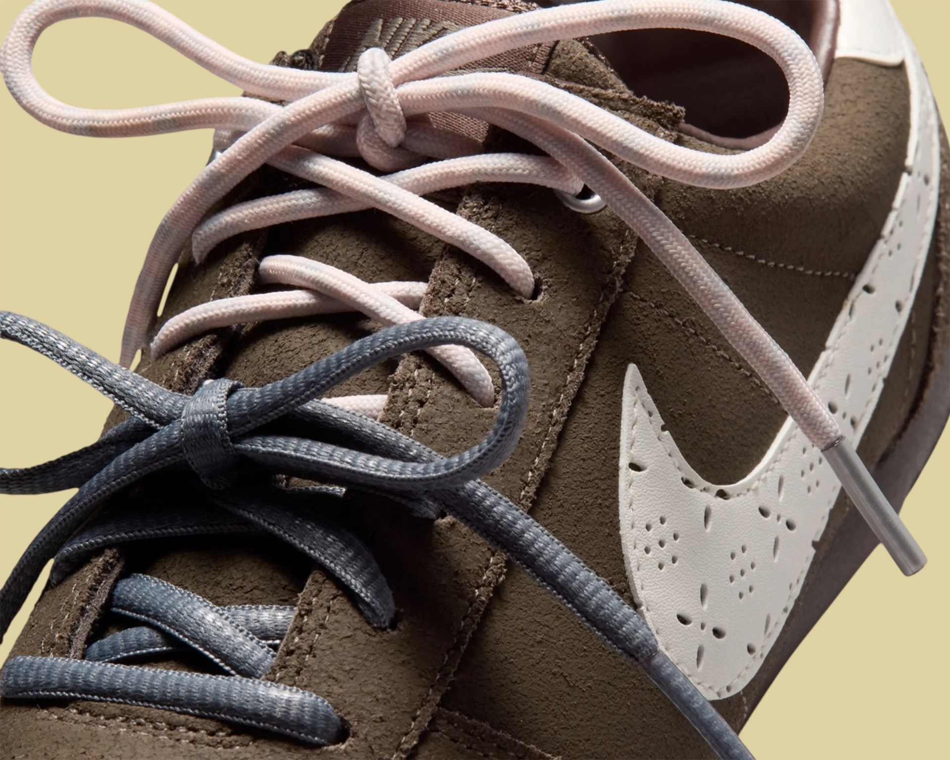 Close-up of brown suede Nike sneaker with white perforated swoosh and two pairs of laces, one pink and one gray.