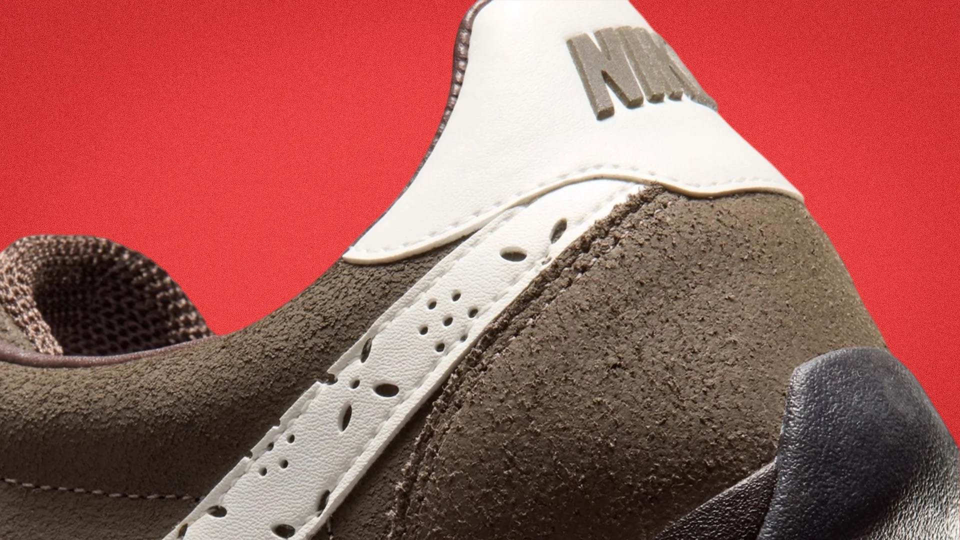 Close-up of a brown suede sneaker heel with white leather accents and a black textured sole against a red background.