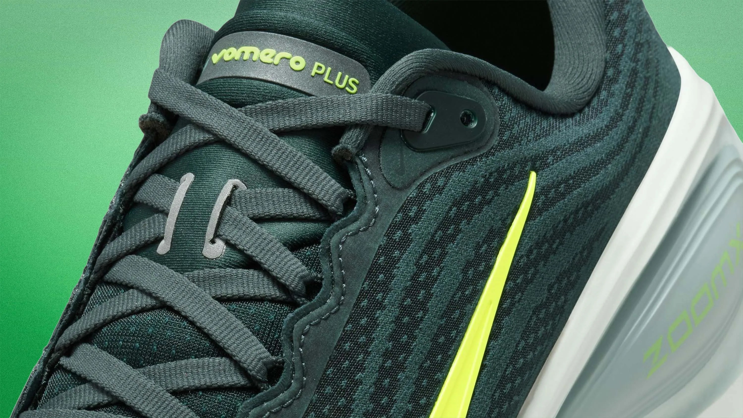 Close-up of a dark green Nike Vomero Plus running shoe with neon yellow swoosh and white sole.