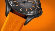 Black chronometer watch with orange accents and an orange textured rubber strap on an orange background.