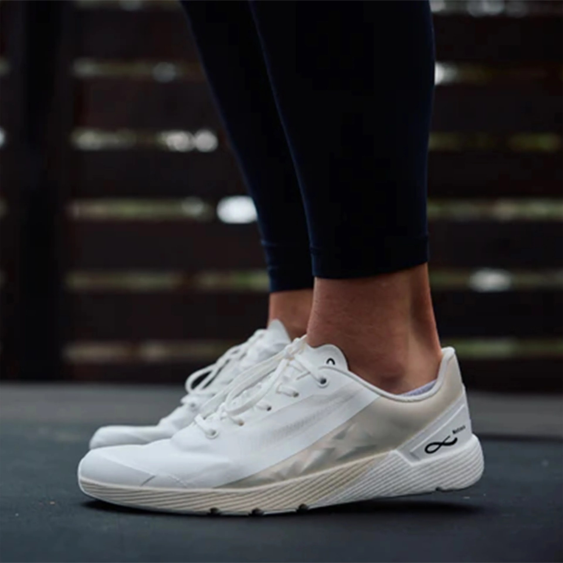White low-top athletic sneakers with laces worn with black leggings on a dark floor.