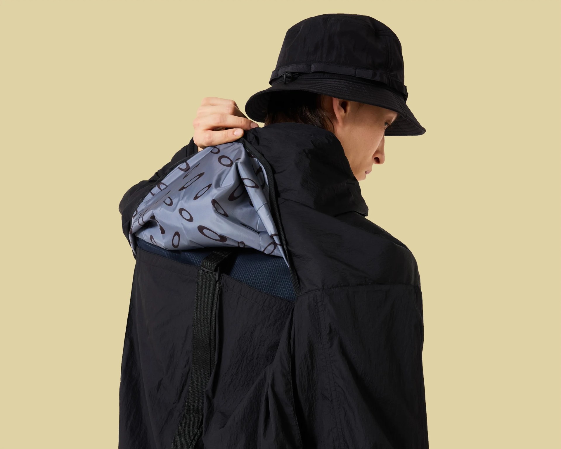Person wearing a black bucket hat and black jacket with a gray hood featuring a repeating oval pattern.