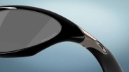 Close-up of black Oakley sunglasses arm with Prizm lens and silver Oakley logo on a blue gradient background.