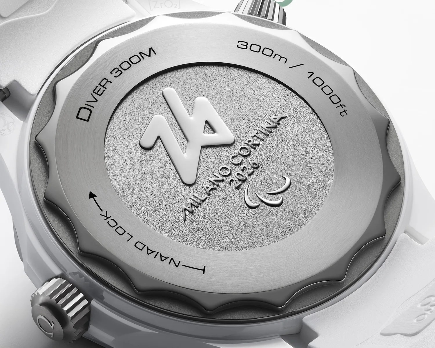 Close-up of a silver watch back with "Diver 300M," "300m / 1000ft," "Milano Cortina 2026," and "Naiad Lock" engravings on a white strap.