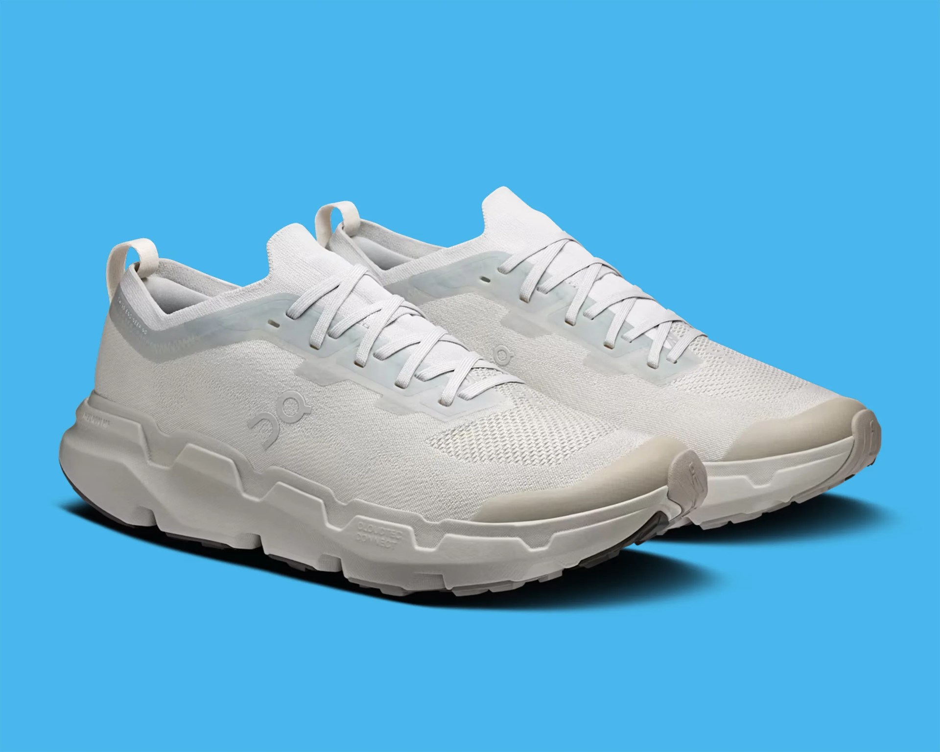 Pair of light gray athletic shoes with thick soles and mesh fabric uppers on a blue background.