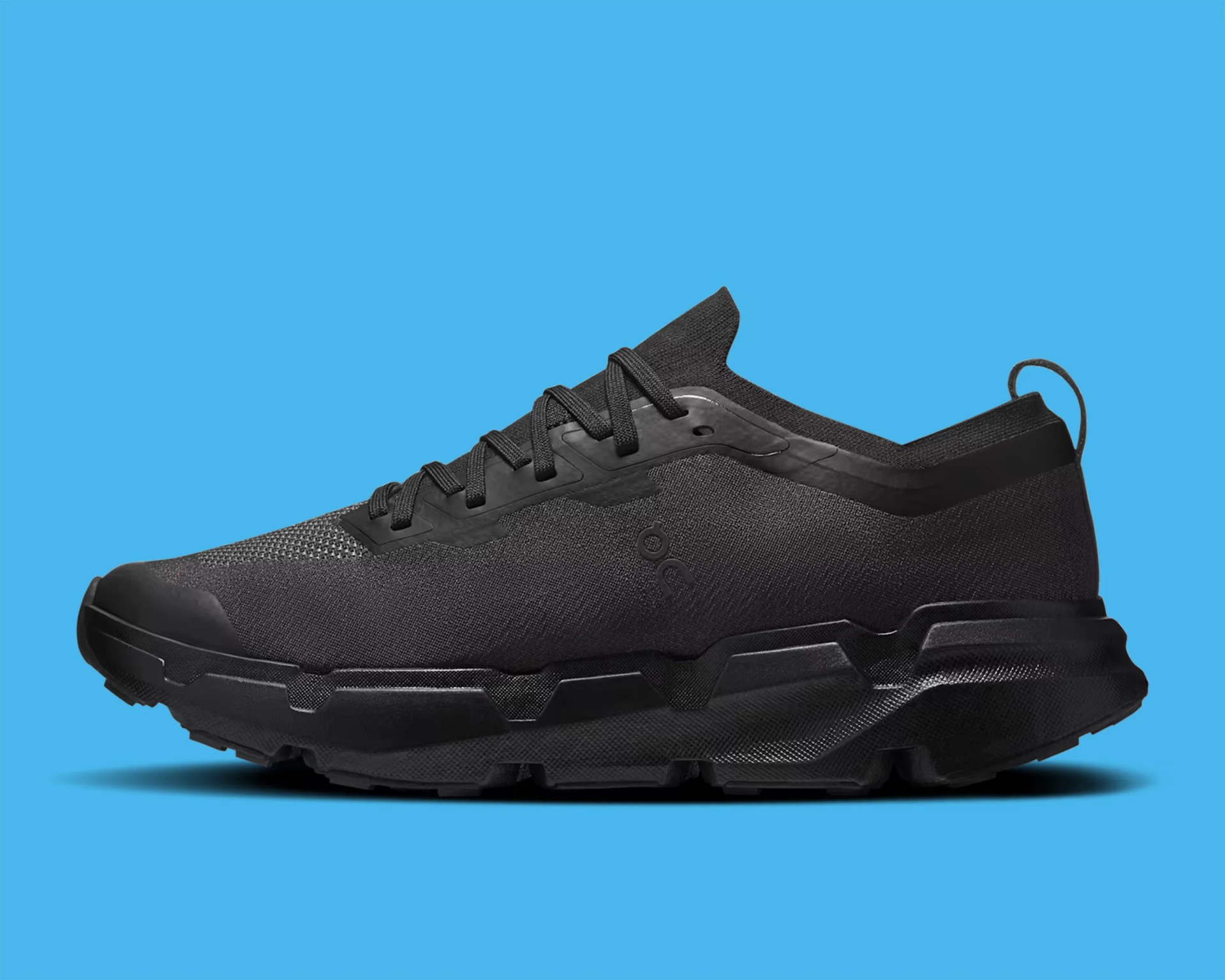 Black athletic sneaker with textured sole and knit upper on a blue background.