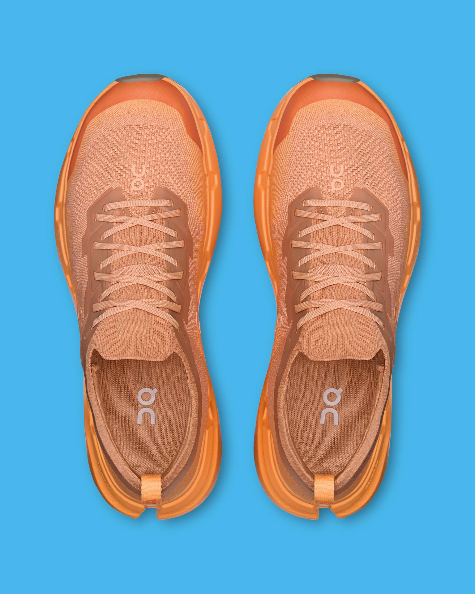 Pair of orange athletic running shoes with knit uppers and thick cushioned soles on a blue background.